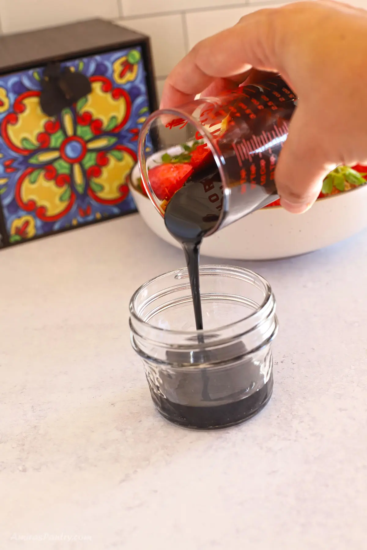 A hand pouring some honey balsamic glaze in a jar.