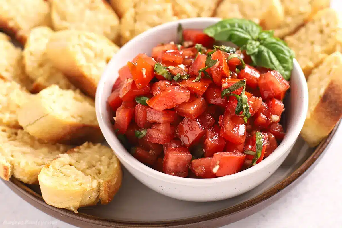 Bruschetta in a bowl with sliced bread on a serving plates.