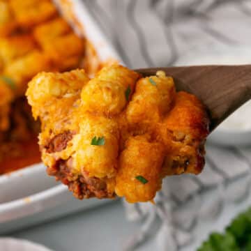 A wooden spoon with a serving of chili tater tot casserole.