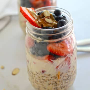A jar with overnight oats garnished with berries and peanut butter.