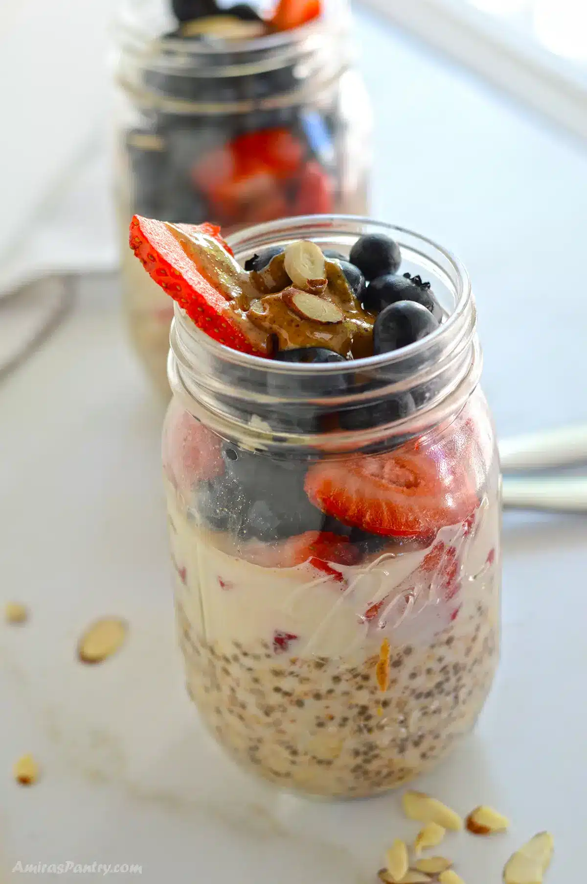 Two jars of overnight oats with berries on a white surface.