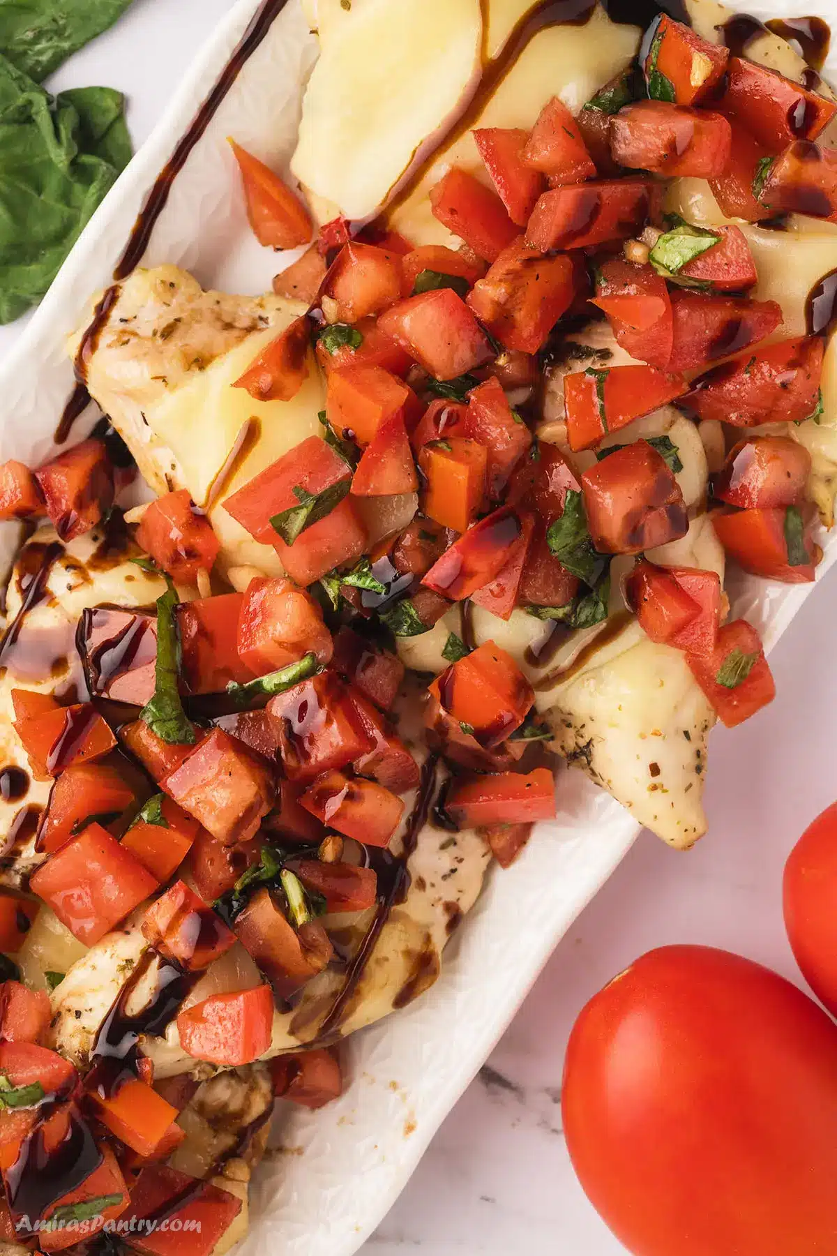Bruschetta chicken on a serving platter topped with tomatoes.