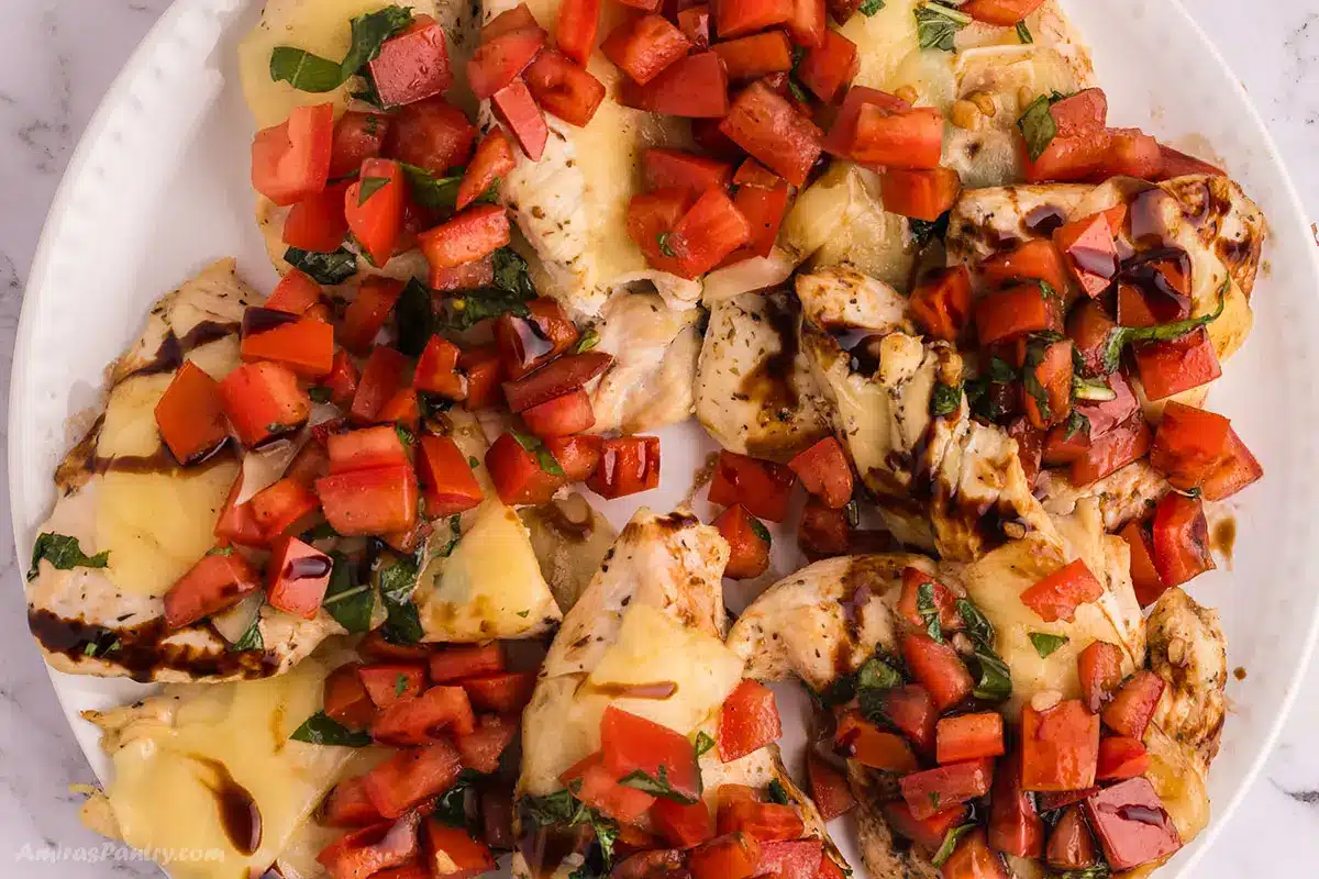 Chicken breasts on a round platter topped with bruschetta mixture.
