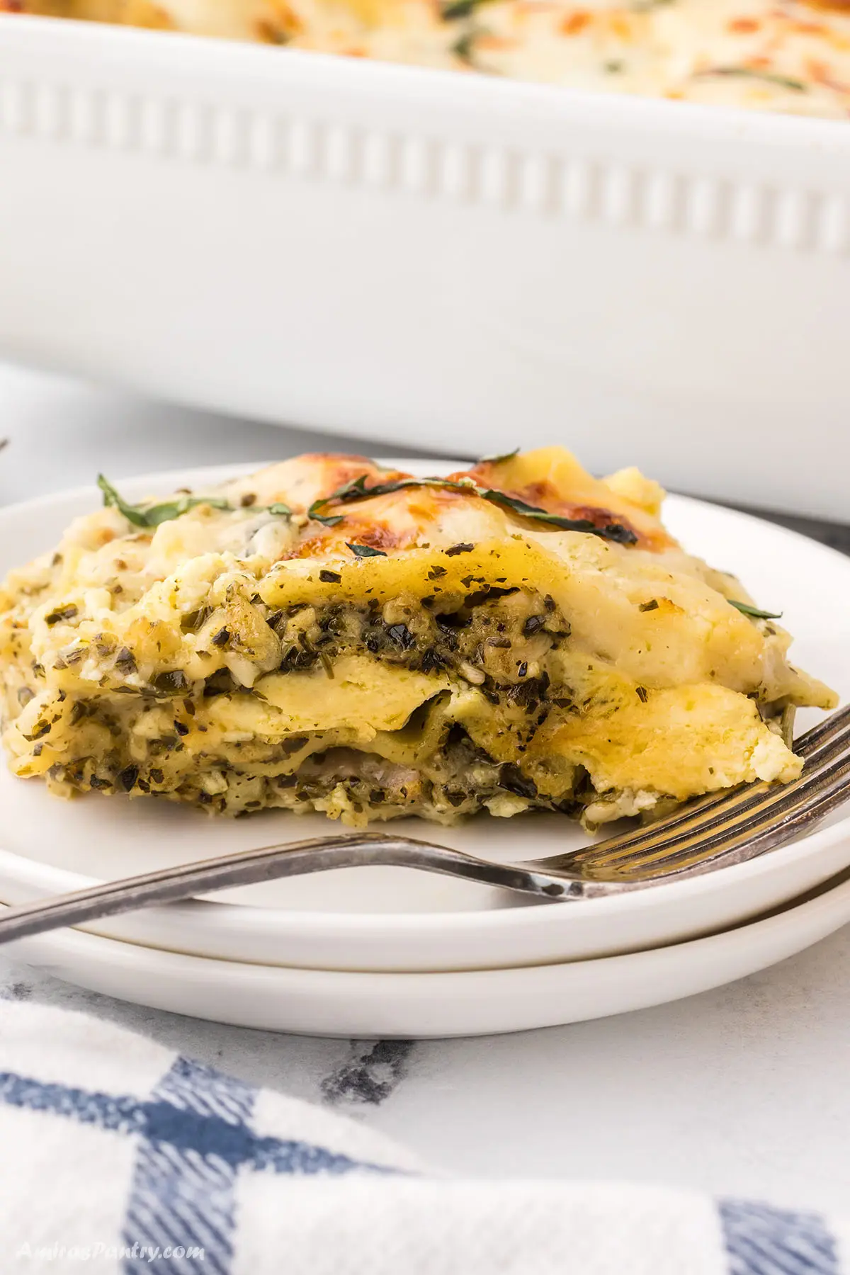 A serving of pesto lasagna on a white dinner plate with a fork.