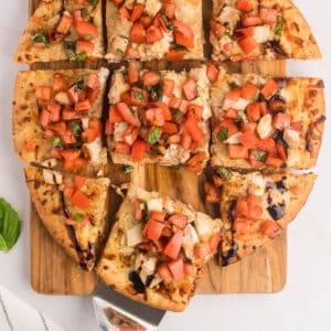 An overhead image of bruschetta pizza with a piece pulled out.