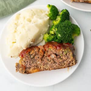 An overhead image of a slice of meatloaf on a dinner plate with mashed potatoes.