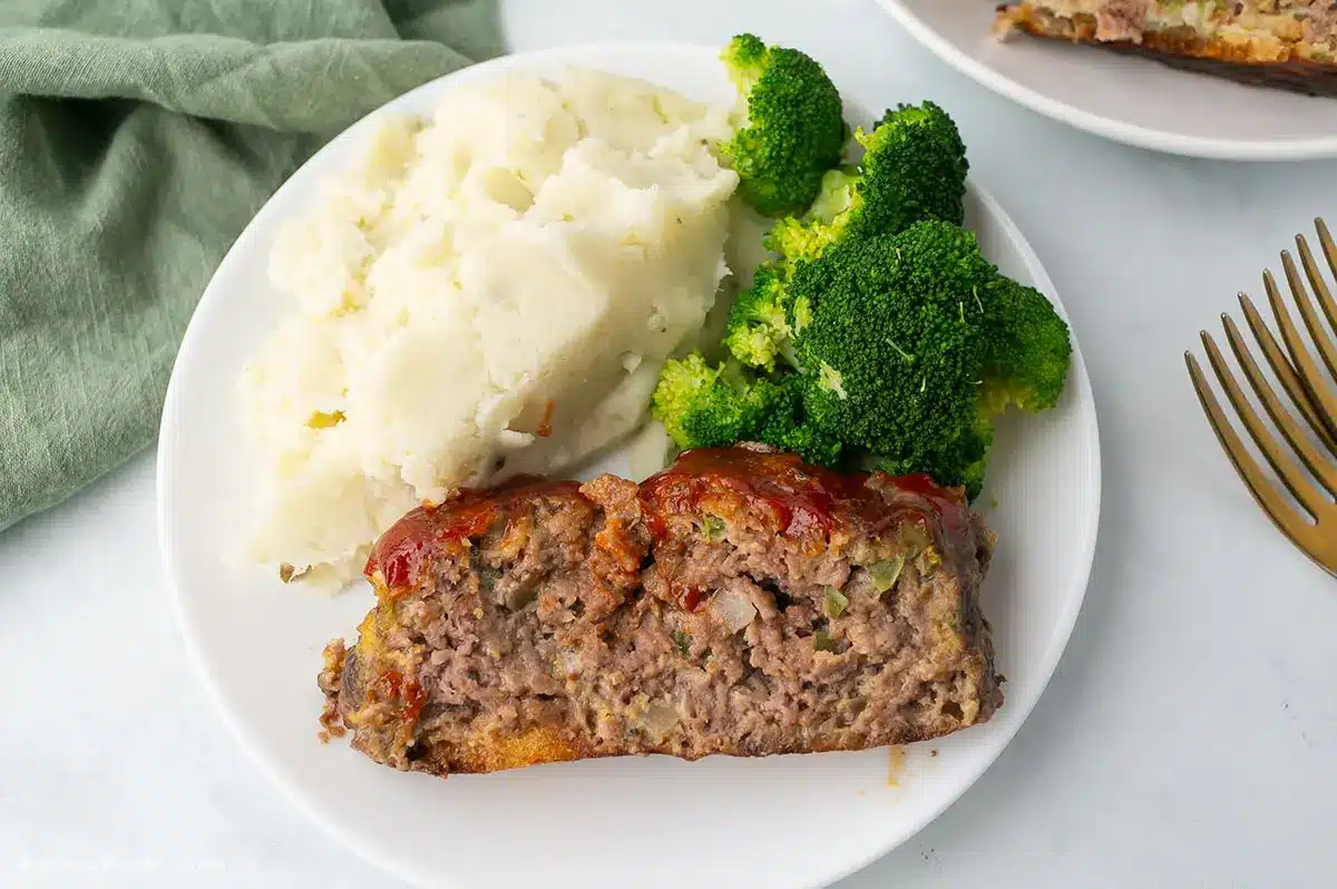 A slice of the meatloaf on a white plate with mashed potatoes.