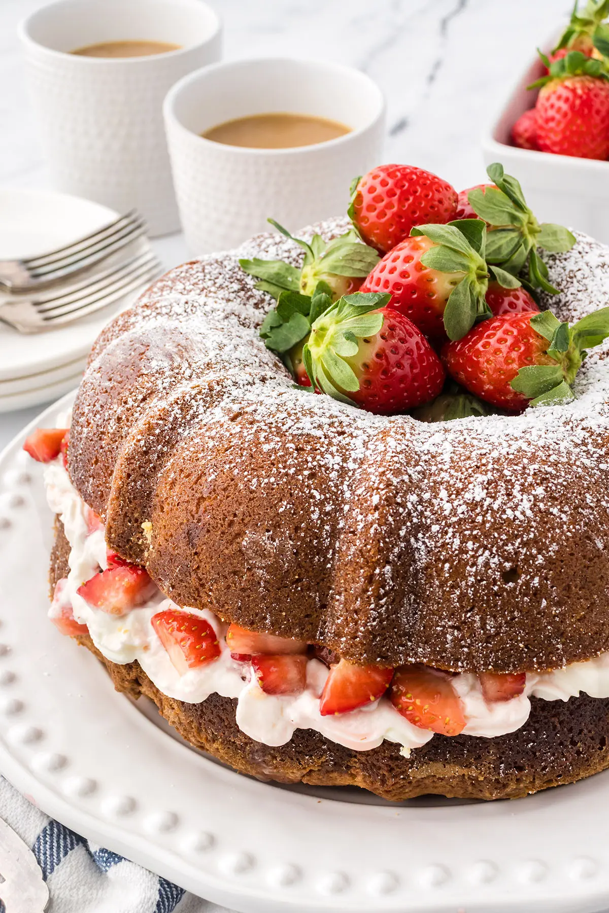 A strawberry shortcake bundt cake filled with whipped cream and topped with fresh strawberries.