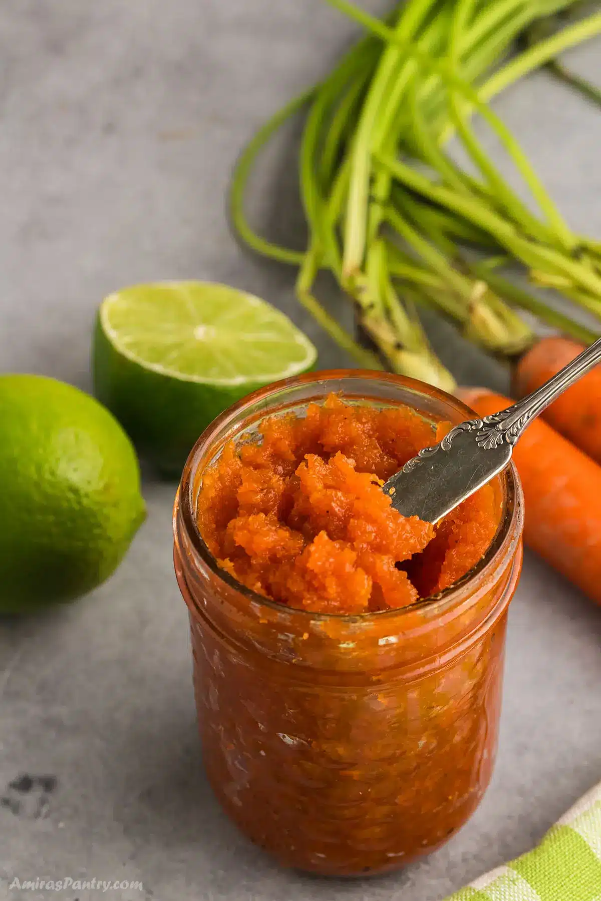 A jar of carrot jam with carrots and lime on the side.