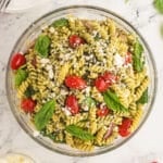 An overhead image of a big glass bowl of chicken pesto salad.