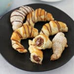 chocolate croissants on a black plate with one cut in half.
