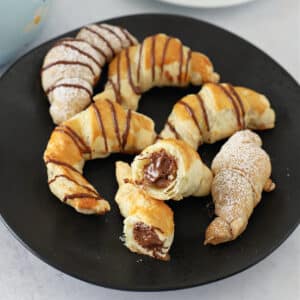 chocolate croissants on a black plate with one cut in half.