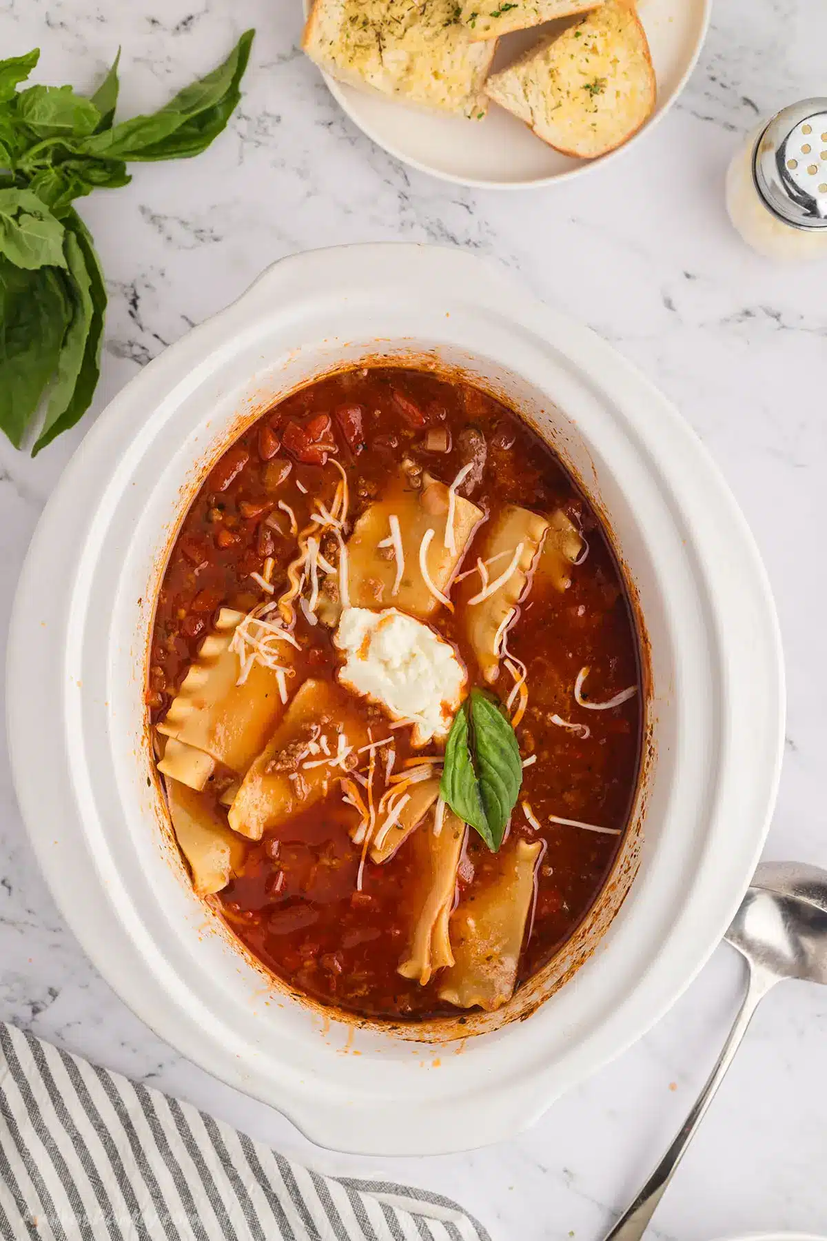 Lasagna soup on a white crockpot garnished with basil leaves.