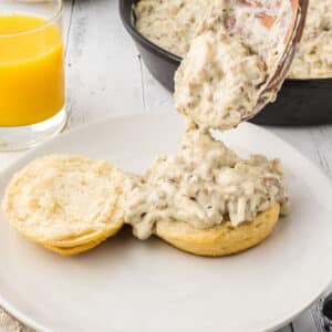 A spoon pouring some turkey sausage gravy on half a biscuit.