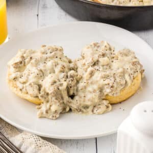A white plate with two biscuit pieces with sausage gravy on top.