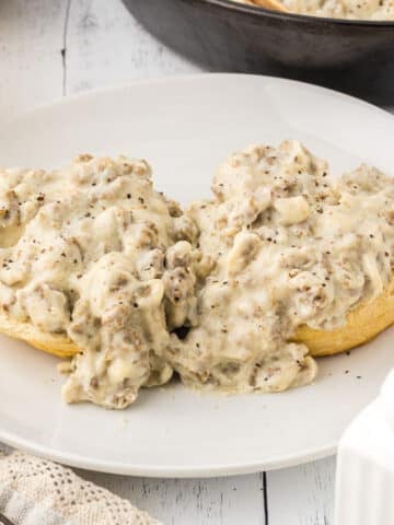 A white plate with two biscuit pieces with sausage gravy on top.