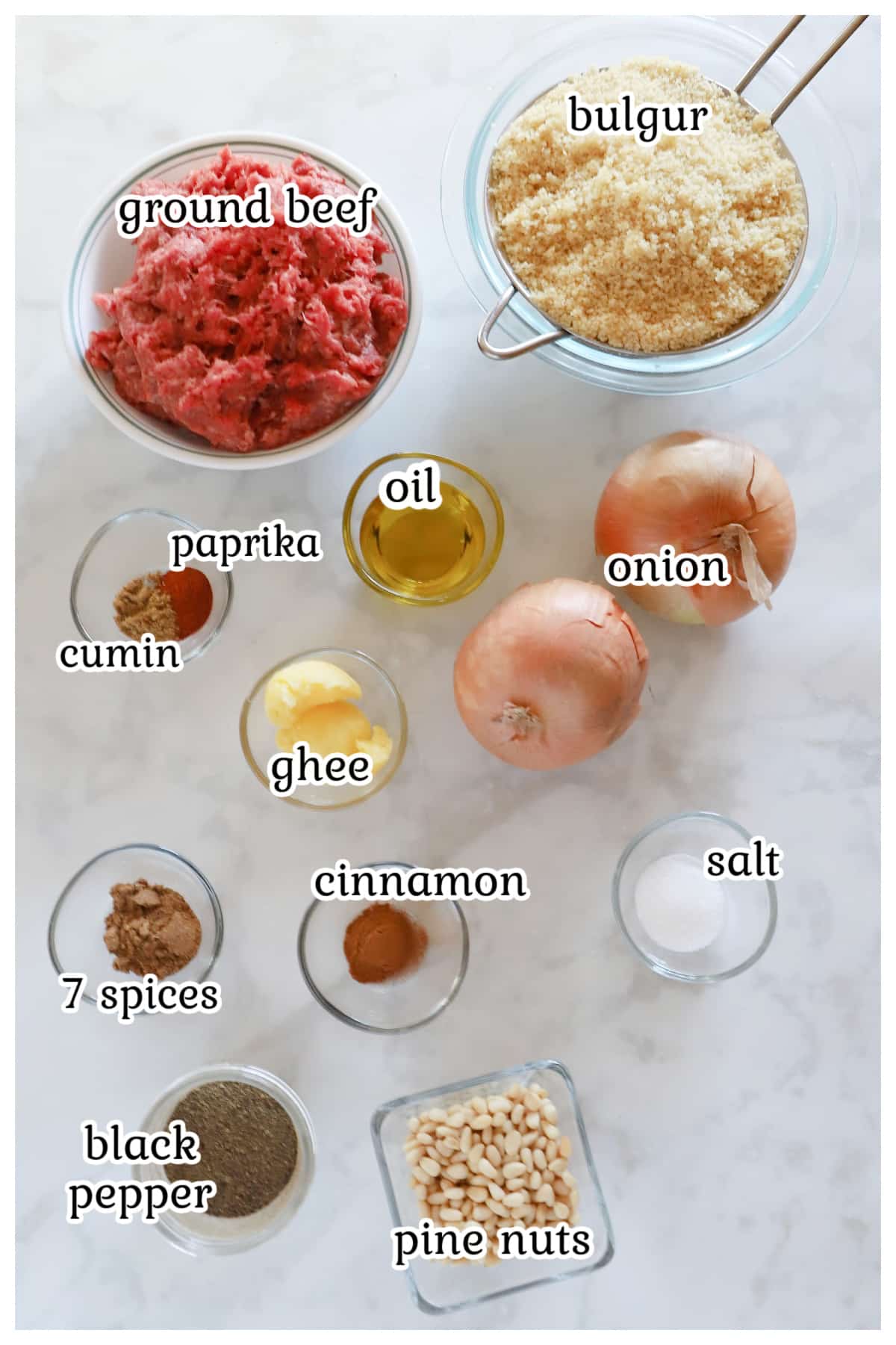 Overhead view of labeled individual ingredients for baked kibbeh arranged on a marble surface.