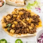 Two beef and potato tacos opened slightly to show inside.