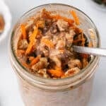 A spoon scooping some carrto cake oats off a glass jar.
