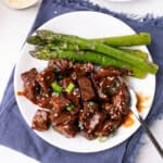 STeak bites ona white plate with steamed asparagus.
