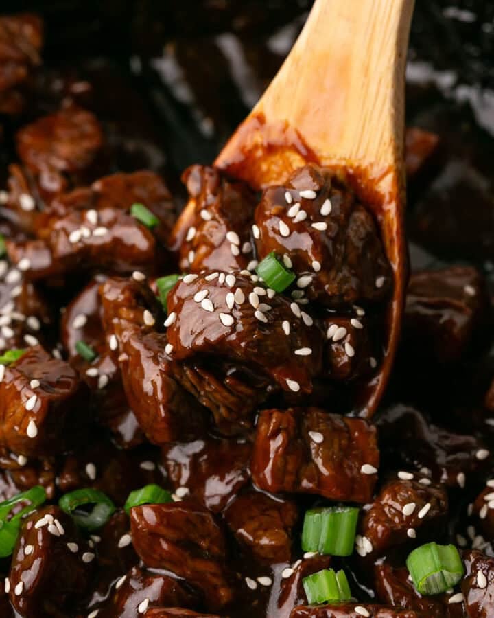 A close up look at honey garlic steak bites in a wooden spoon.