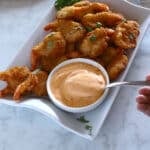 A small metal spoon with some sauce in a shrimp platter.