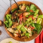 A wooden bow with chicken fajita salad with a spoon.