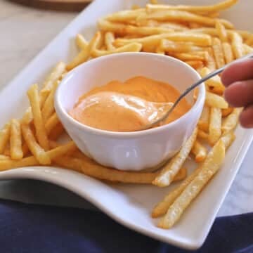 A spoon dipped in a bowl of creamy sriracha sauce.
