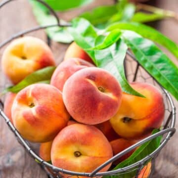 A basket filled with fresh peaches on a wooden surface.