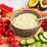 A brown bowl with green avocado sauce with a spoon in the bowl.