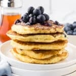 Lemon ricotta pancakes on a whote plate with syrup in the back.