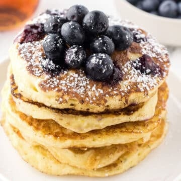 Lemon blueberry pancakes on a white plate topped with fresh blueberries.