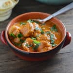 An overhead view of a bowl with chicken tikka masala on a wooden surface.