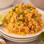 A serving of rice on a white plate with a lime wedges.