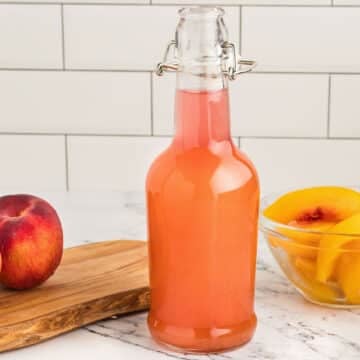 A close up on a glass bottle filled with peach syrup.