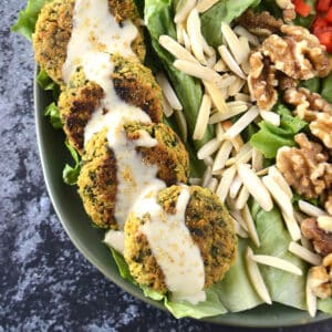 Baked falafel arranged on a green plate drizzled with tahini.