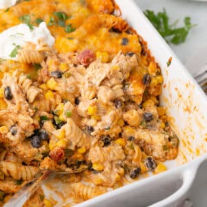 A chicken fiesta on a white casserole with part taken from it to show inside.