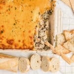 An overhead image of a casserole with crab spinach dip and some bread slices on the side.