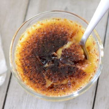 A glass ramekin with creme brulee with a spoon in it.