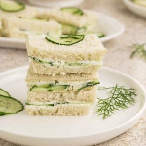 A stack of dill cucumber sandwiches garnished with cucumber slices and dill.