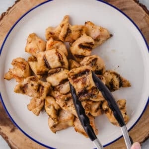 A kitchen tonge with a piece of grilled chicken nuggets.