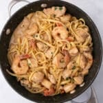 An overhead image of a large skillet with alfredo pasta with shrimp and chicken.