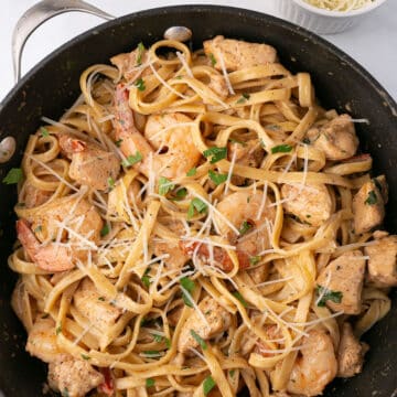 A dark skillet with Alfredo pasta with chicken and shrimp.