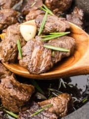 A wooden spoon scooping some steak bites with garlic and rosemary butter.