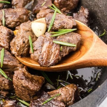 A wooden spoon scooping some steak bites with garlic and rosemary butter.