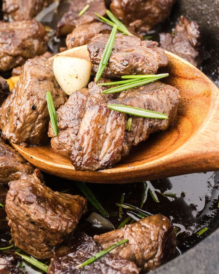 A wooden spoon scooping some steak bites with garlic and rosemary butter.