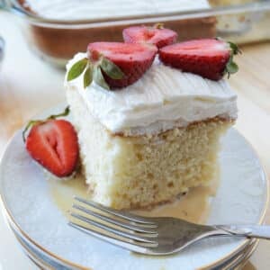 A close up image of a dessert plate with a piece of tres leches cake with fresh strawberries.