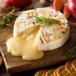 A brie wheels on a wooden surface oozing with cheese.