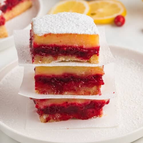A stack of cranberry lemon bars separated with parchment paper.