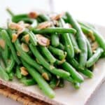 A white plate with green beans and almonds.